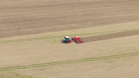 Agricultural tractor pulling wide seeding equipment through dry cultivated field Stock Footage 345501170