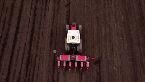 Agricultural tractor with red seed drill is actively planting seeds in freshly Stock Footage 325197953