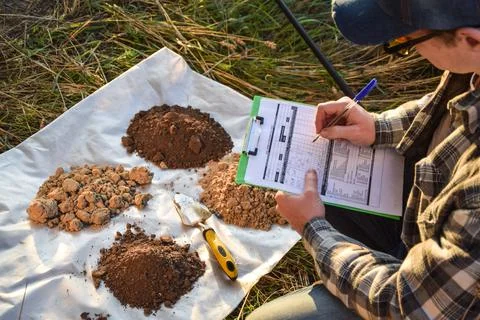 Agriculturist taking notes in soil sampling information sheet at field Stock Photos
