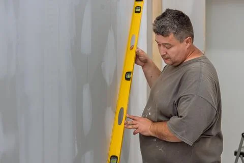 With the aid of a level, the employee checks the equalization of the drywall Stock Photos