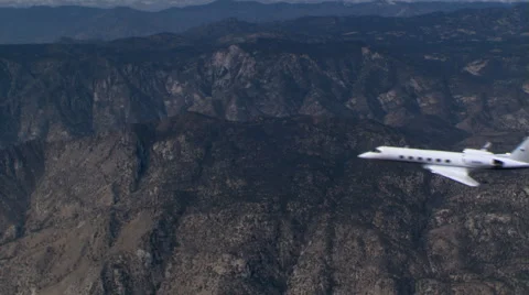 Air-to-air side view of executive jet over rugged terrain Stock Footage 59477320