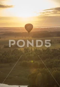 An air balloon flying over the field and trees using heat technology - bright Stock Photos