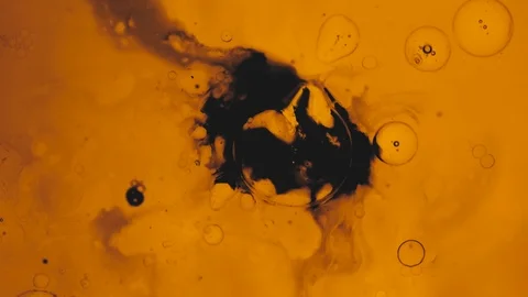 Air bubbles explode near a patch of black ink in a yellow liquid Stock Footage 119814958