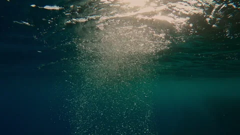 Air bubbles rise to surface of rippling sea in evening light, backlighting Stock Footage 339964476