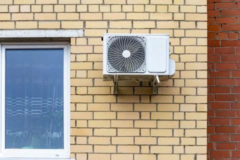 An air conditioning system installed outside on the wall of a brick building. Stock Photos