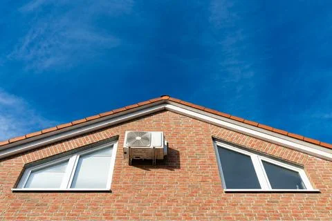 Air conditioning unit mounted on a brick house under a clear sky Stock Photos