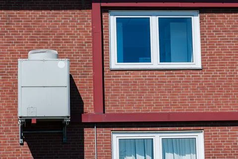 Air conditioning unit mounted on a brick wall near windows Stock Photos