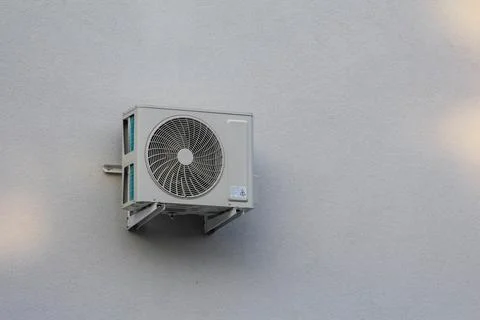 Air conditioning unit mounted on gray wall in urban setting during daytime Stock Photos