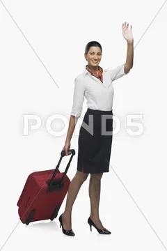Air hostess carrying her luggage and waving Stock Photos