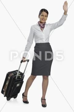 Air hostess carrying her luggage and waving Stock Photos
