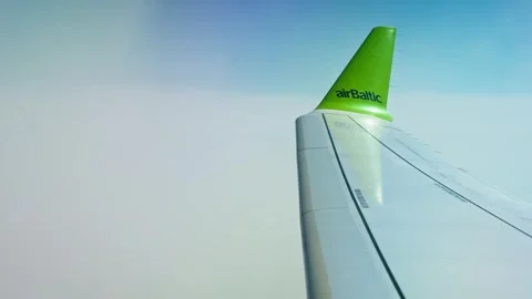 AirBaltic airplane wing above soft white clouds, with green winglet logo, blue Stock Footage 336291589