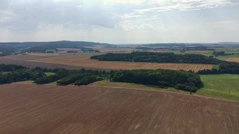 Airborne view over patchwork farmland: brown plowed fields, green hedgerows, and Stock Footage 348504209