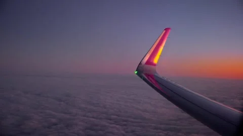 Aircraft cruising above cloud layer at sunset with glowing wingtip view. Window Stock Footage 336544666