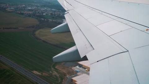 Aircraft wing and engine in flight over green fields and industrial area, Video stock 328481009