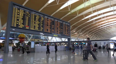 Airline passengers walk past schedule board in departure lobby Shanghai airport Stock Footage 67545444