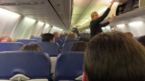Airline stewardess closes overhead bin while passengers board an airplane cabin Stock Footage 256248321