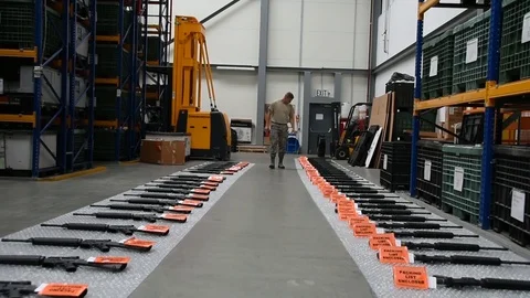 Airman checking rifles laid out in line on bubblewrap at warehouse Stock Footage 111998207