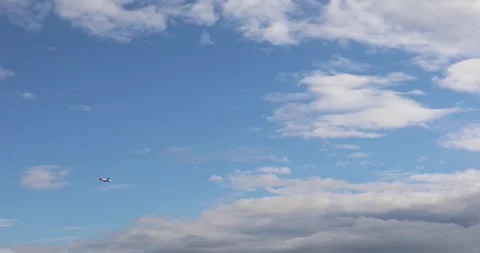 Airplane in blue sky with scattered clouds above soft horizon Stock Footage 320030027