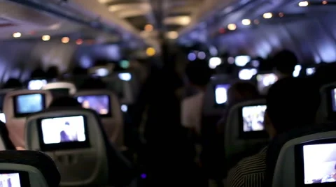 Airplane cabin interior with tv screens, passengers seated flying toward LAX Stock Footage 44113497