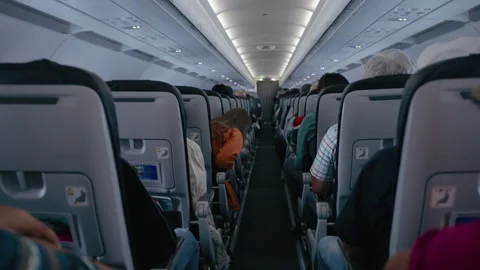 Airplane cabin interior view down aisle with seated passengers during flight. Stock Footage 338367381