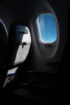 Airplane cabin window next to empty seat blue sky weather strong contrast Fotos de archivo