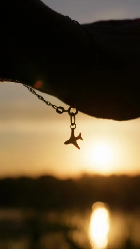 Airplane Charm Bracelet Dangling Against Sunset Over Water Silhouette Stock Footage 345424388