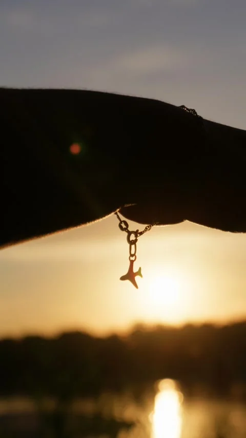 Airplane Charm Bracelet Dangling from Hand During Golden Hour Sunset Stock Footage 345424434