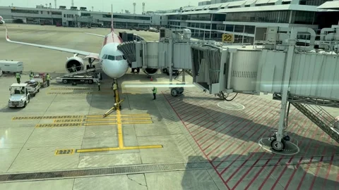 Airplane docked at jet bridge with ground crew and vehicles at airport gate Stock Footage 233283258