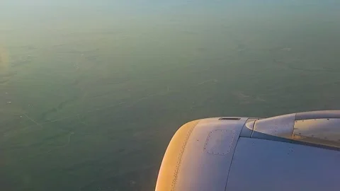 Airplane engine and wing view over farmland beneath stormy clouds and glowing 動画素材 334601689
