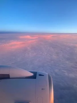 Airplane engine is visible through cockpit window. Blue sky and pink-orange d Stock Photos