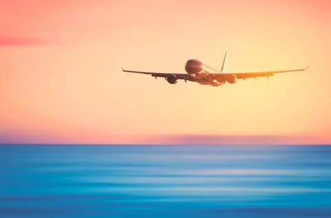 Airplane flying over blur tropical beach and sunset sky abstract background.  Stock Photos