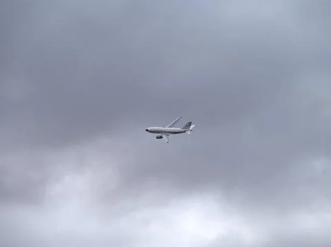 Airplane flying in the sky under a cloudy gray overcast day Stock Photos