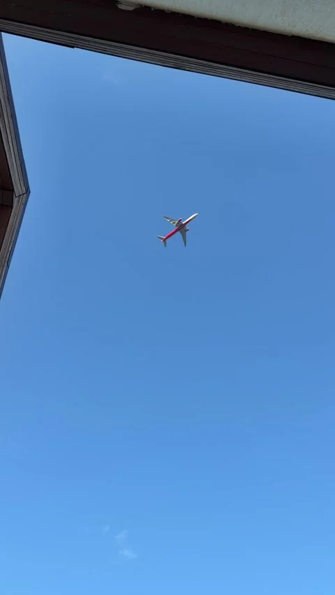 Airplane flying through a clear blue sky, captured from below a building's roof Stock Footage 338275998