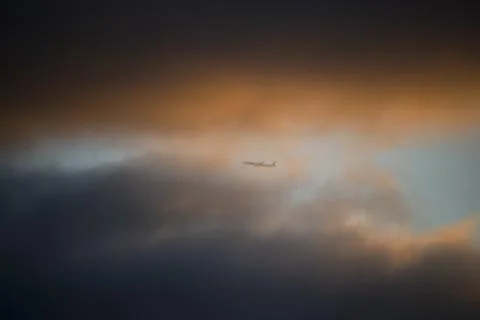 Airplane flying through dramatic clouds at sunset Photos