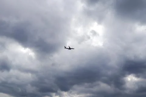 Airplane flying through dramatic cloudy sky, silhouetted against a moody ba.. Stock Photos