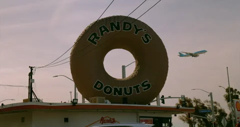 Airplane flying through the giant Randy’s Donuts sign in Los Angeles Stock Footage 342727667