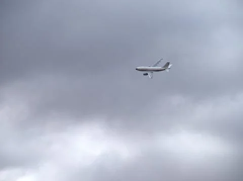 Airplane flying through a grey cloudy sky Stock Photos