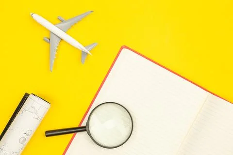 Airplane model, notebook, map and magnifier on yellow background, flat lay. Stock Photos