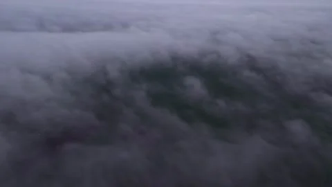Airplane Side Window Shot Over Dense Cloud Layer and Green Landscape Below Stock Footage 337008692