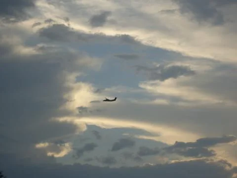 Airplane silhouette flies through dramatic cloudy sky with golden sunlight Stock Photos