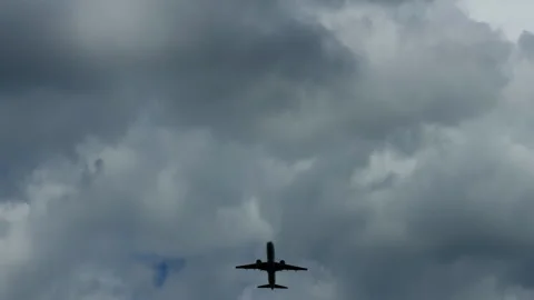 Airplane silhouette flying beneath dramatic storm clouds over blue sky with open Stock Footage 345763203