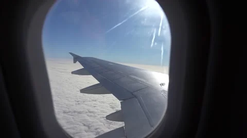 Airplane small window view during flight above blue sky with clouds and sunflare Stock Footage 219743114
