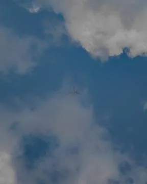 Airplane soaring through white clouds in a bright blue sky 写真素材