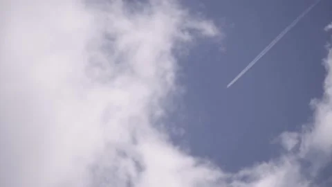 An airplane with white trails cross the blue sky with cotton candy clouds Stock Footage 137322828