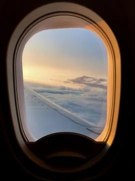 Airplane window frames clouds and wing during a calm evening flight. Soft s.. Stock Photos