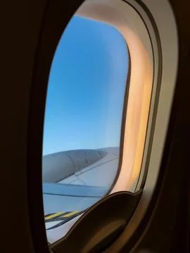 Airplane window frames clouds and wing during a calm evening flight. Soft s.. Stock Photos