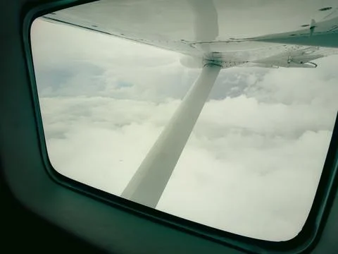 Airplane window frames a view of clouds and a propeller Stock Photos