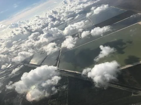 Airplane window looking down on many clouds and farmland. Stock Photos