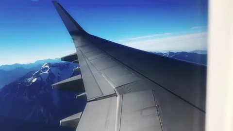 Airplane window with sky clouds and mountains and people in seats Stock Footage 247160011