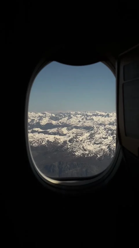 Airplane window view of endless snowy mountain range under blue sky Stock Footage 346559788